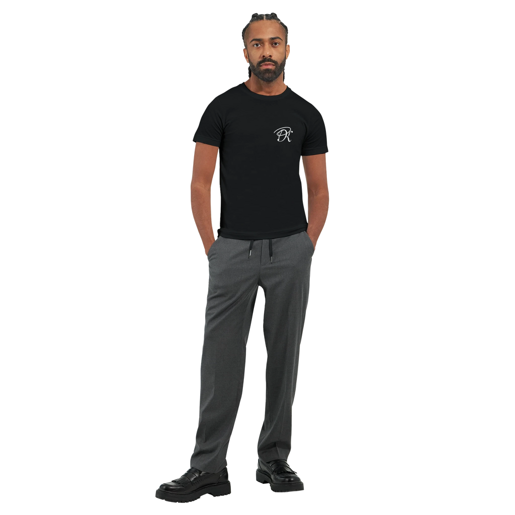 Male model wearing a black “Color the Grey” unisex T-shirt with a subtle white PK monogram on the front, styled with grey trousers in a clean full-body look.
