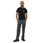 Male model wearing a black “Color the Grey” unisex T-shirt with a subtle white PK monogram on the front, styled with grey trousers in a clean full-body look.