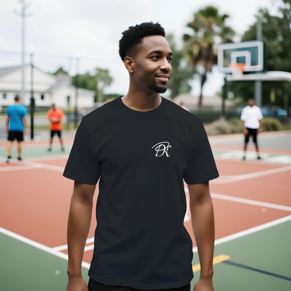 Male model wearing a black unisex statement T-shirt with a small white PK monogram on the chest, styled in a casual outdoor streetwear setting.