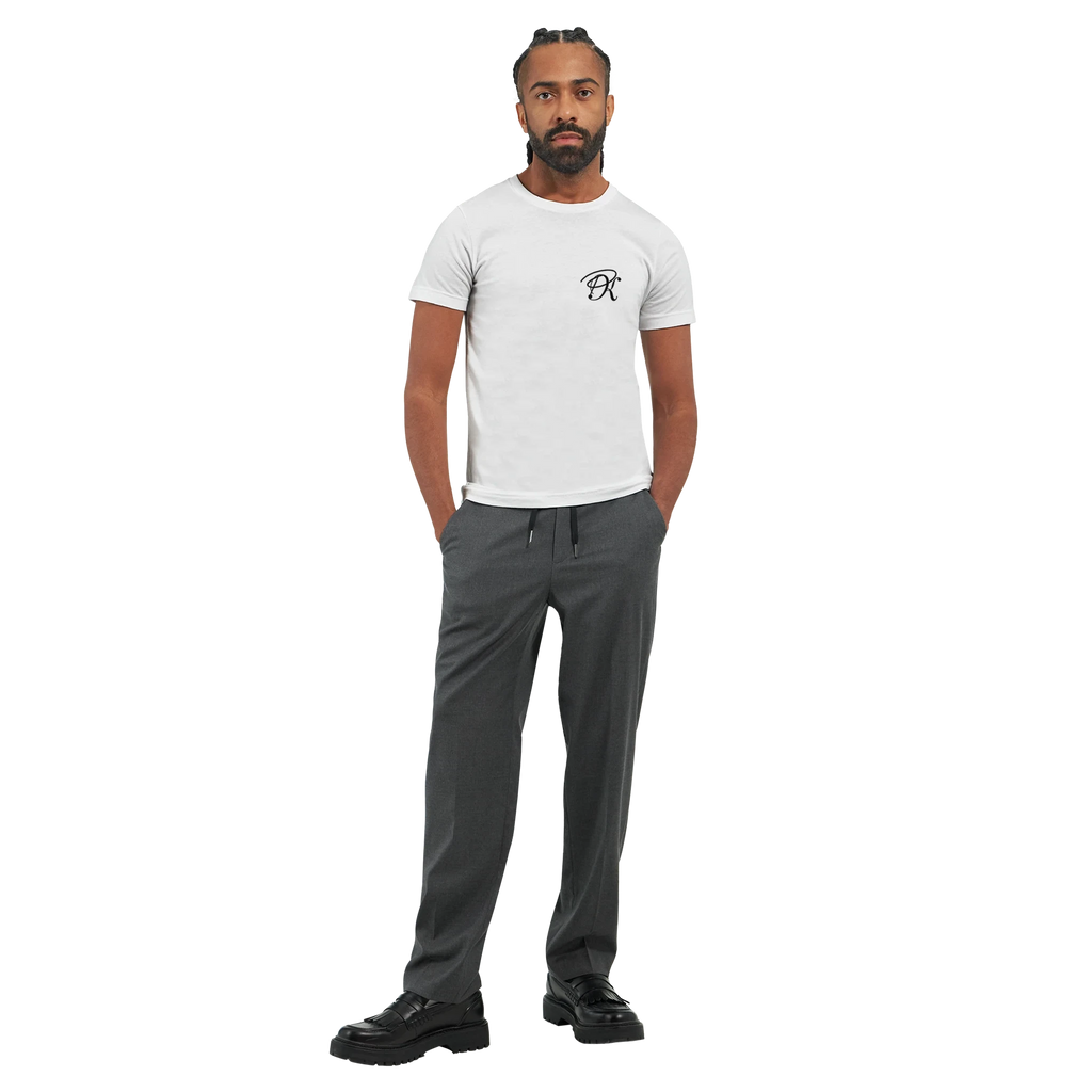 Male model wearing a white T-shirt with a small black PK logo on the chest, shown in a full-body front view with dark grey trousers for a clean, modern unisex streetwear look.