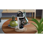 15oz stainless steel travel mug with a surreal shattered vintage clock design displayed on a wooden coffee table in a modern living room. The black-and-white artwork is accented with vibrant rainbow powder splashes, while plants and decorative vases create a warm, contemporary setting.