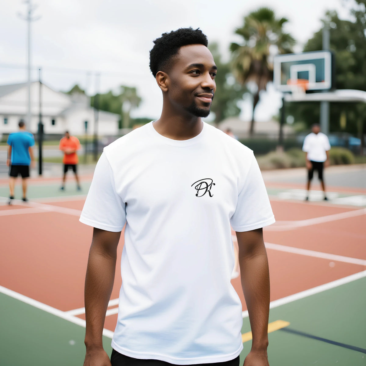 Male model wearing a white T-shirt with a small black PK logo on the chest, shown outdoors on a basketball court for a casual, modern streetwear look.