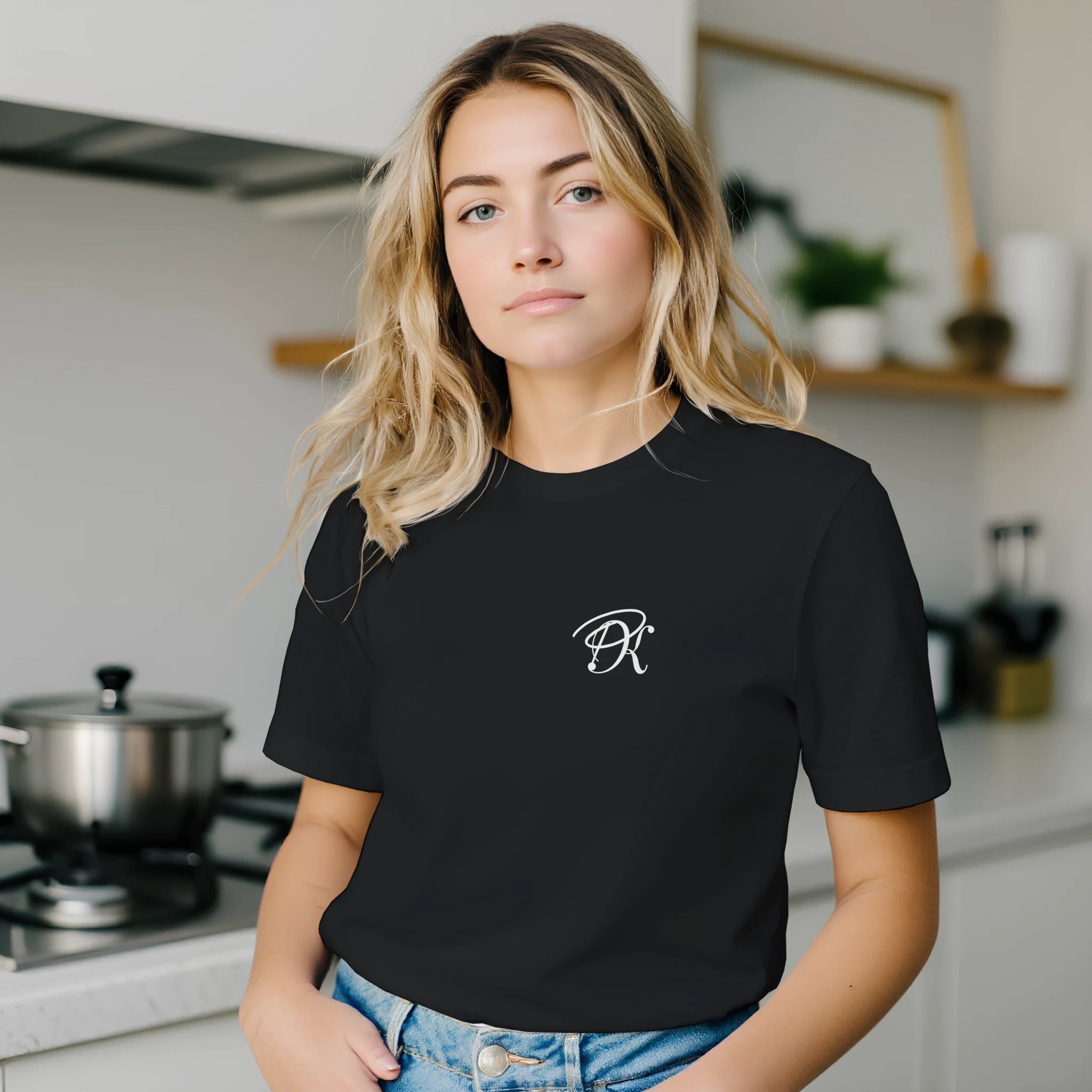 Female model wearing a black unisex statement T-shirt with a small white PK monogram on the chest, styled with denim jeans in a casual everyday setting.