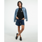 Female model wearing a black unisex statement T-shirt with a small white PK monogram on the chest, styled with a denim jacket and shorts for a casual streetwear look.
