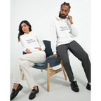 Male and female models wearing matching white hoodies with the black “You Were Never Ordinary” statement design, seated together in a clean studio setting with neutral trousers and black shoes.