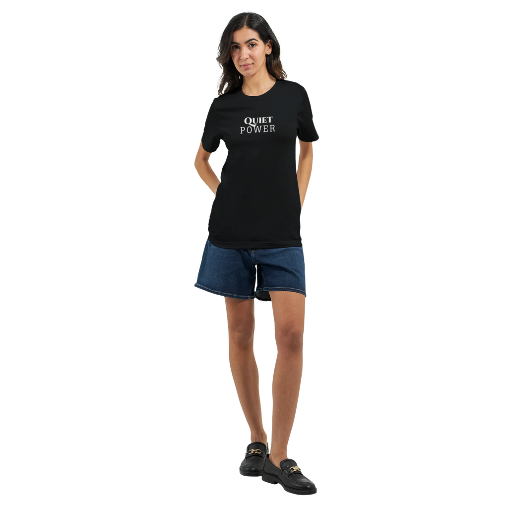 Full-body female model wearing a black unisex T-shirt with the small white “QUIET POWER” chest print, styled with dark denim shorts and black shoes.