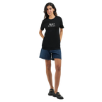 Full-body female model wearing a black unisex T-shirt with the small white “QUIET POWER” chest print, styled with dark denim shorts and black shoes.