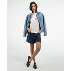 Female model wearing a white T-shirt with a small black PK logo on the chest, layered with a blue denim jacket and paired with denim shorts and black shoes for a casual, modern streetwear look.
