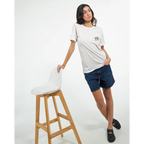Female model wearing a white T-shirt with a small black PK logo on the chest, paired with denim shorts and black shoes in a clean studio setting for a casual unisex streetwear look.
