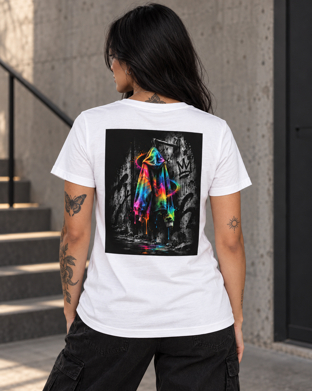 Female model shown from behind wearing a white T-shirt with a bold neon rainbow hoodie back print against a black-and-white graffiti background, styled with black cargo trousers for an expressive urban streetwear look.