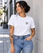Female model wearing a white T-shirt with a small black PK logo on the chest, styled with blue jeans and visible tattoos in a modern urban setting for a clean, contemporary streetwear look.
