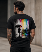 Tattooed male model wearing a black “Color the Grey” T-shirt from the back, featuring a monochrome woman with umbrella and vibrant neon rainbow graffiti city artwork.