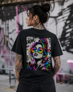 Tattooed female model wearing a black NEON REBEL unisex T-shirt, shown from the back with a large black-and-white graffiti artwork and vibrant neon rainbow accents.