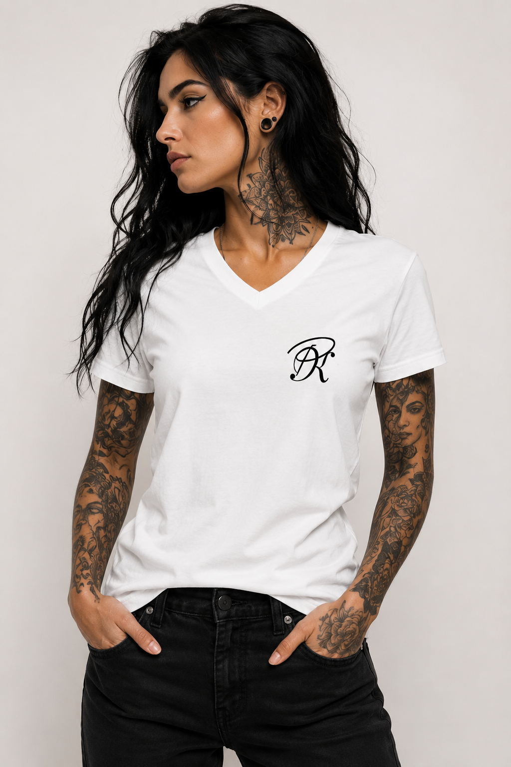 Front view of a tattooed woman with long black hair wearing a white unisex V-neck T-shirt with a small black PK monogram on the left chest, styled with black jeans.