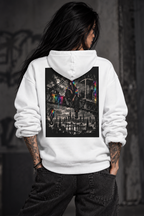 Tattooed female model shown from behind wearing a white hoodie with a large black-and-white urban crane cityscape back print and selective neon rainbow accents, paired with relaxed black jeans.