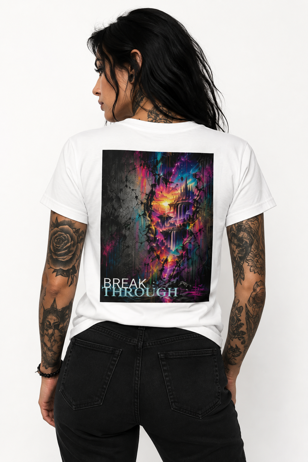 Tattooed woman with long black hair wearing a white T-shirt featuring the colorful “BREAK THROUGH” abstract artwork as a large back print, styled with black jeans.