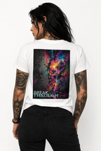 Tattooed woman with long black hair wearing a white T-shirt featuring the colorful “BREAK THROUGH” abstract artwork as a large back print, styled with black jeans.